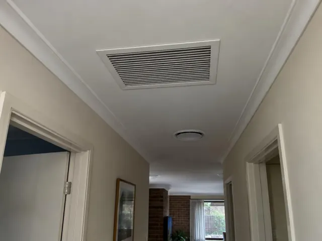 Ceiling return-air grille in a hallway with beige walls and white trim in Elizabeth