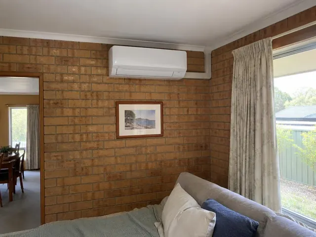Split system indoor unit on a brick wall in a living room with window and curtains in Elizabeth Park